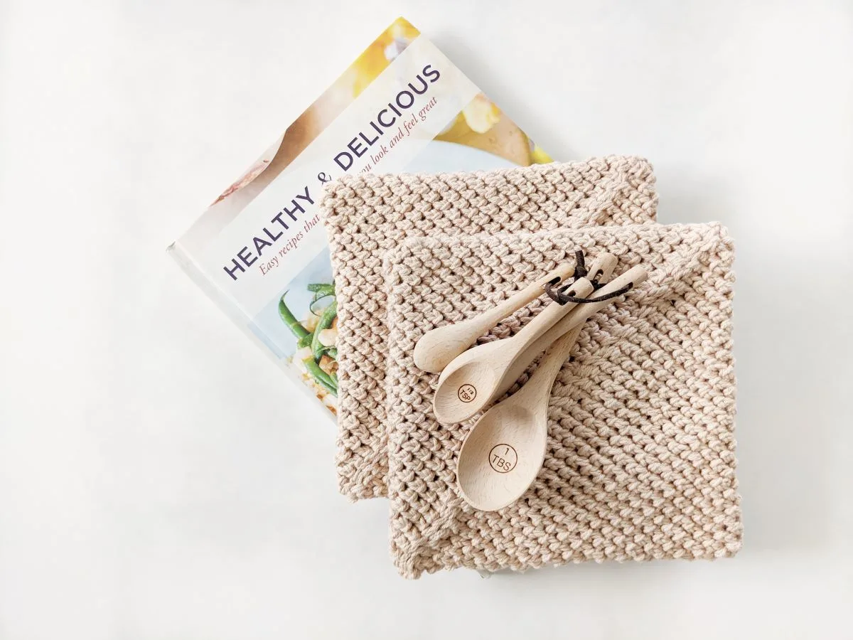 a stack of double thick crochet potholders with measuring spoons and a cookbook