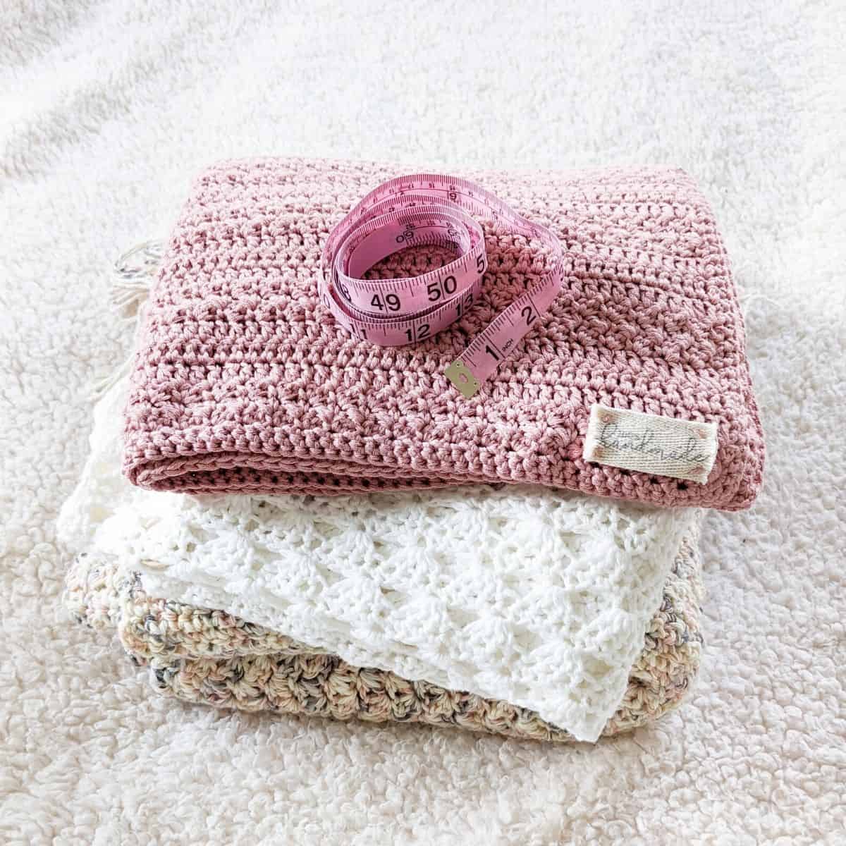 crochet blankets stacked on top of each other with a tape measurer