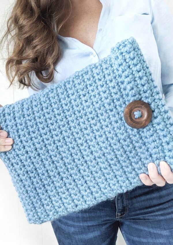 model is holding a chunky crochet laptop cover with a big button