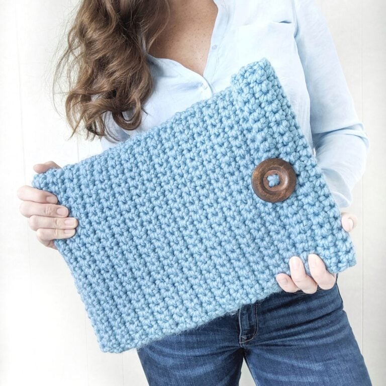 model is holding a chunky crochet laptop cover with a big button