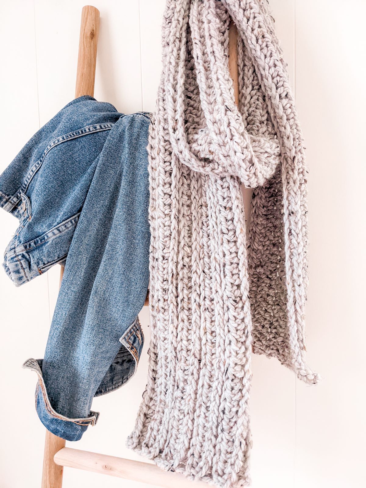 A chunky crochet scarf in the color grey draped on a decorative ladder.
