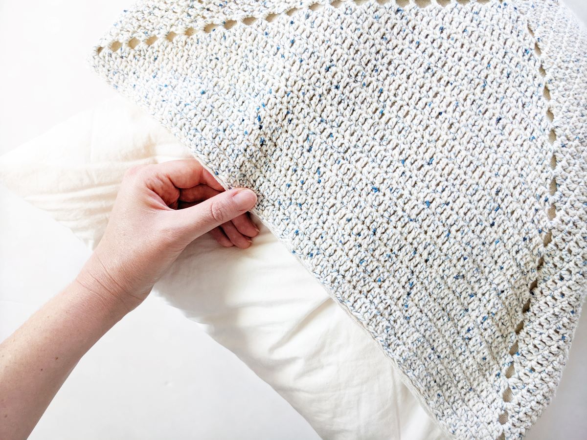 image shows a pillow being put into a granny square cushion cover