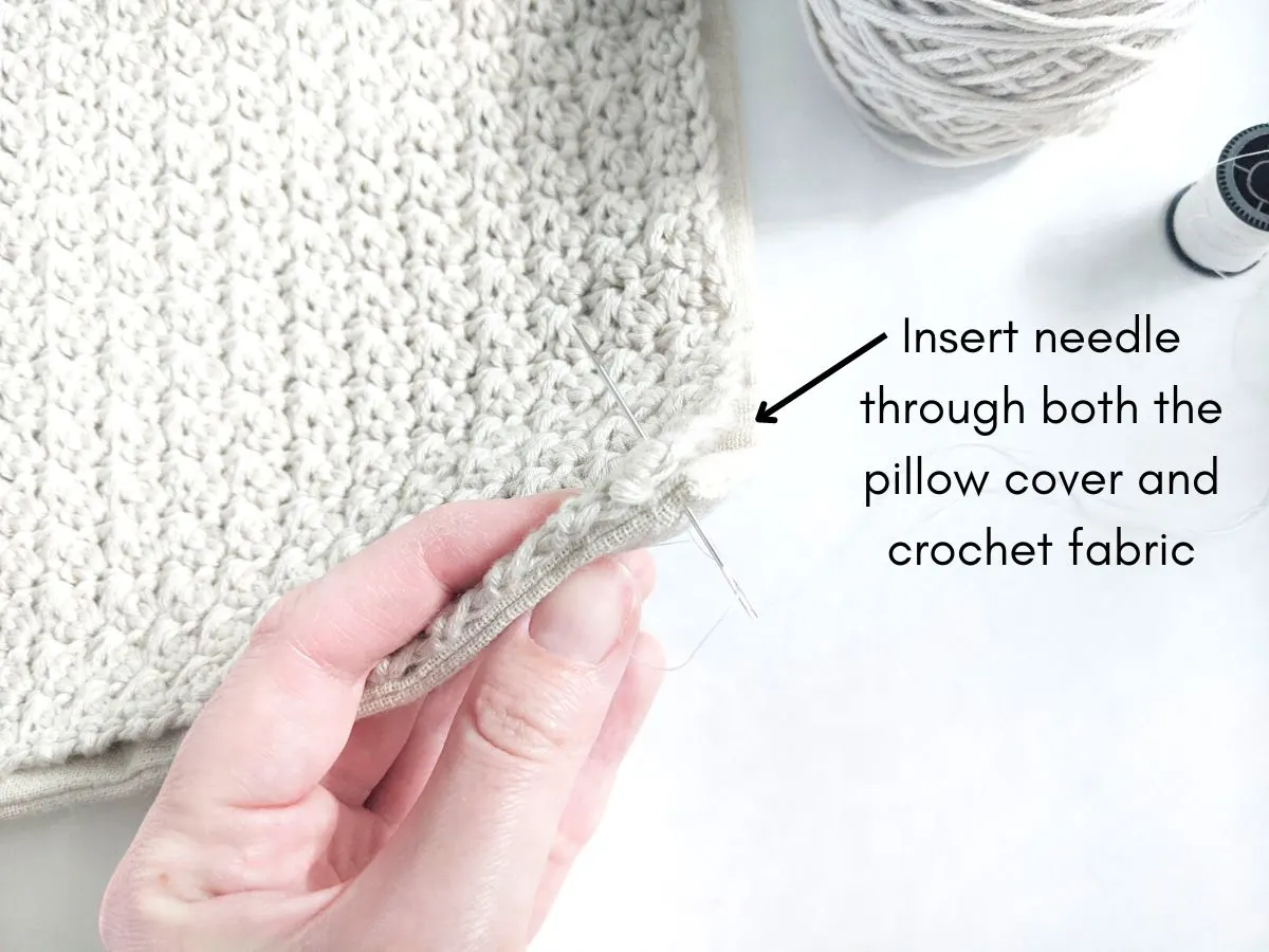 A needle being inserted through the pillow cover and crochet panel. 