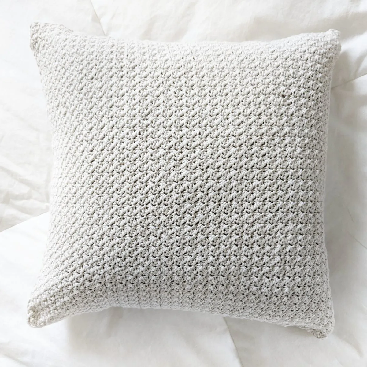 A farmhouse style crochet pillow on a bed.