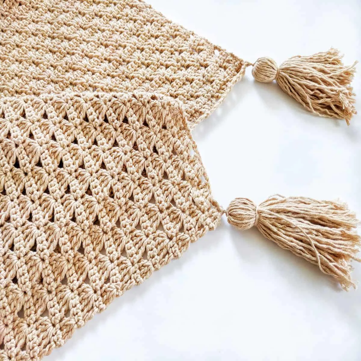 a crochet blanket with two cotton bamboo tassels on a white surface