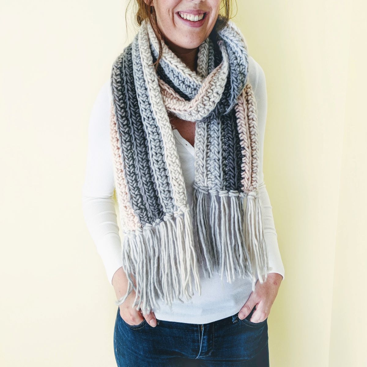 a person wearing a chunky crochet scarf with a white shirt and a pair of jeans