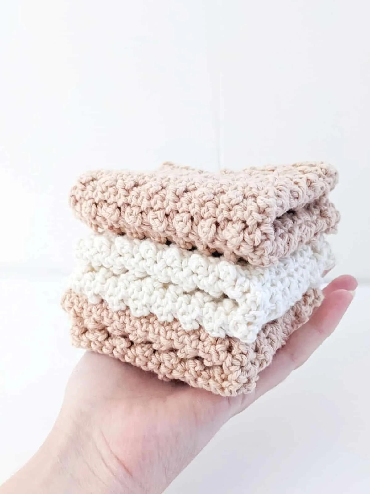 model holding 3 folded crochet dishcloths in the color white and linen