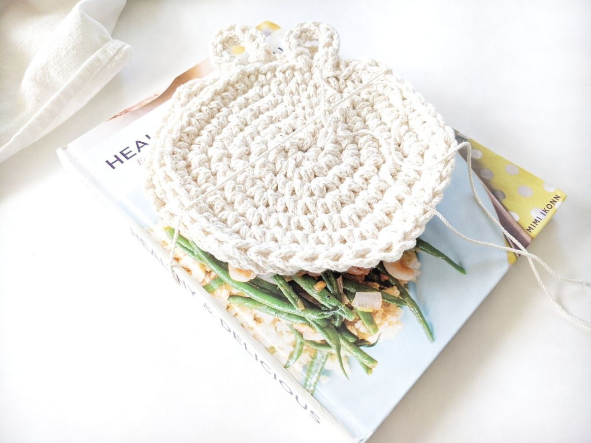 double thick cotton crochet hot pads are on a top of a cook book and tied together with twine