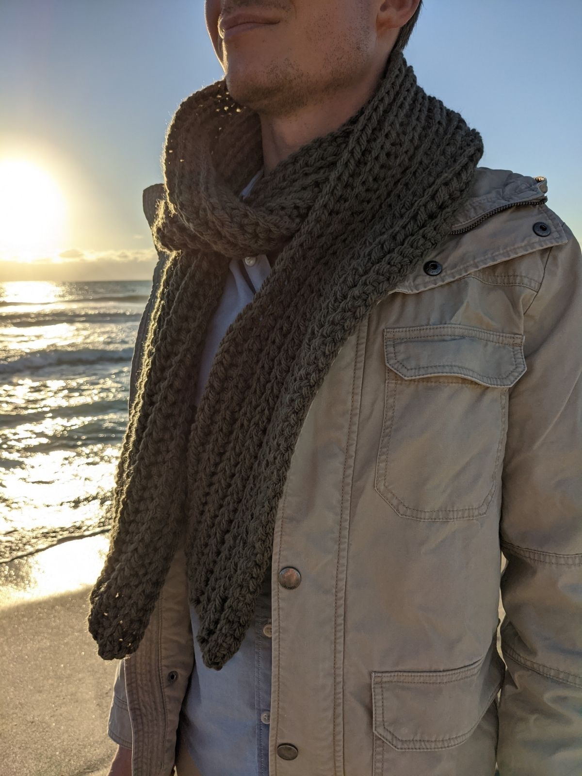 Gentleman is wearing a ribbed crochet scarf that is wrapped around his neck. 