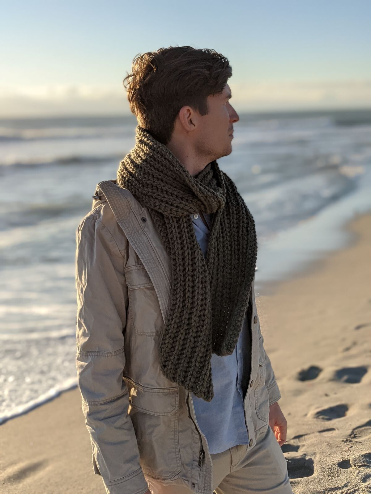 model is wearing a long ribbed men's crochet scarf in the color fatigues a Hue + Me Lion Brand yarn