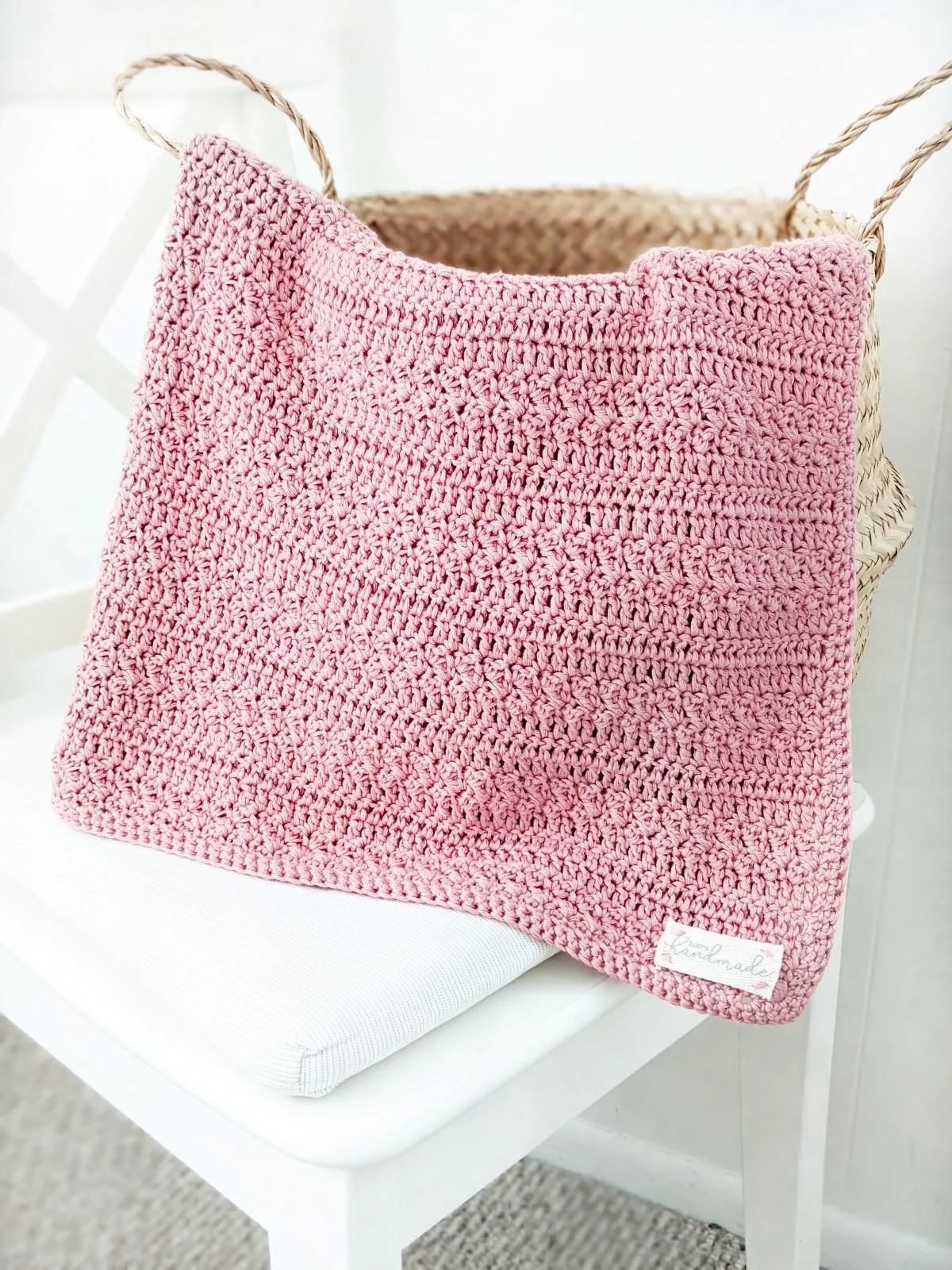 an easy cotton crochet baby girl blanket in a belly basket on a white chair