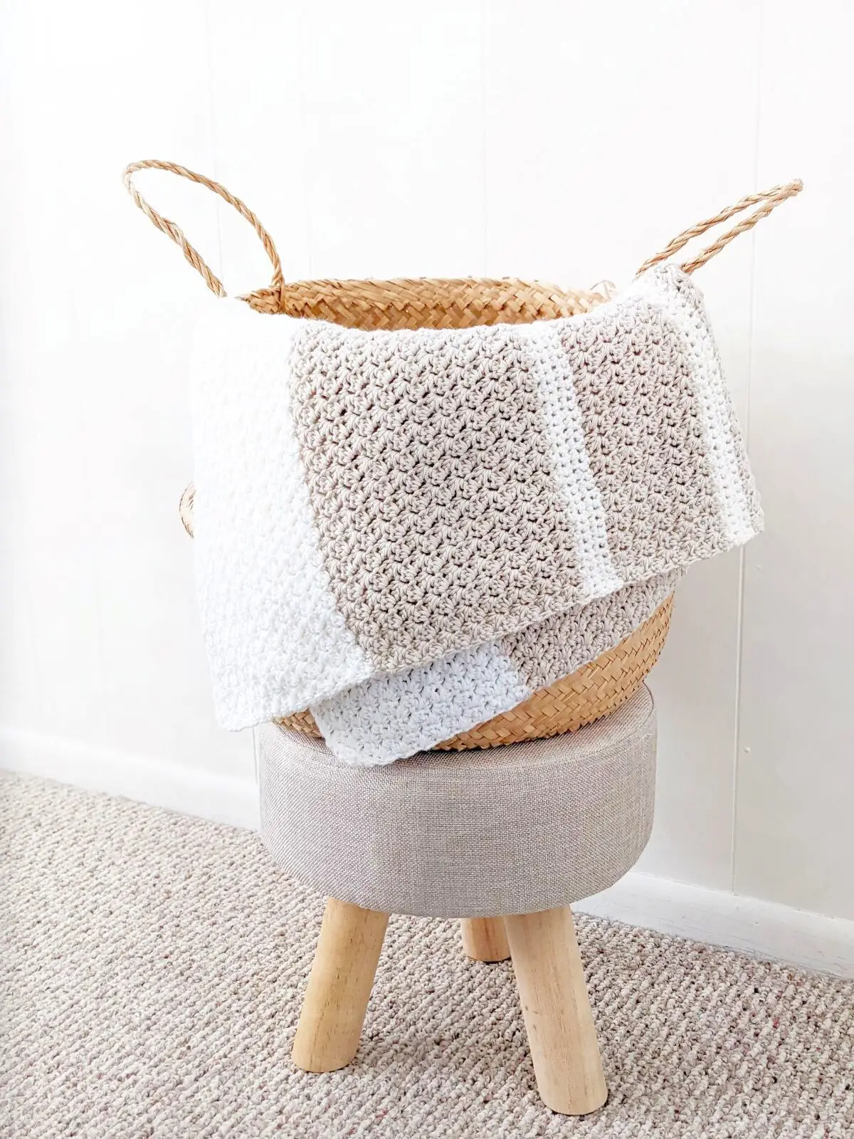 A folded striped crochet baby blanket in a belly basket.
