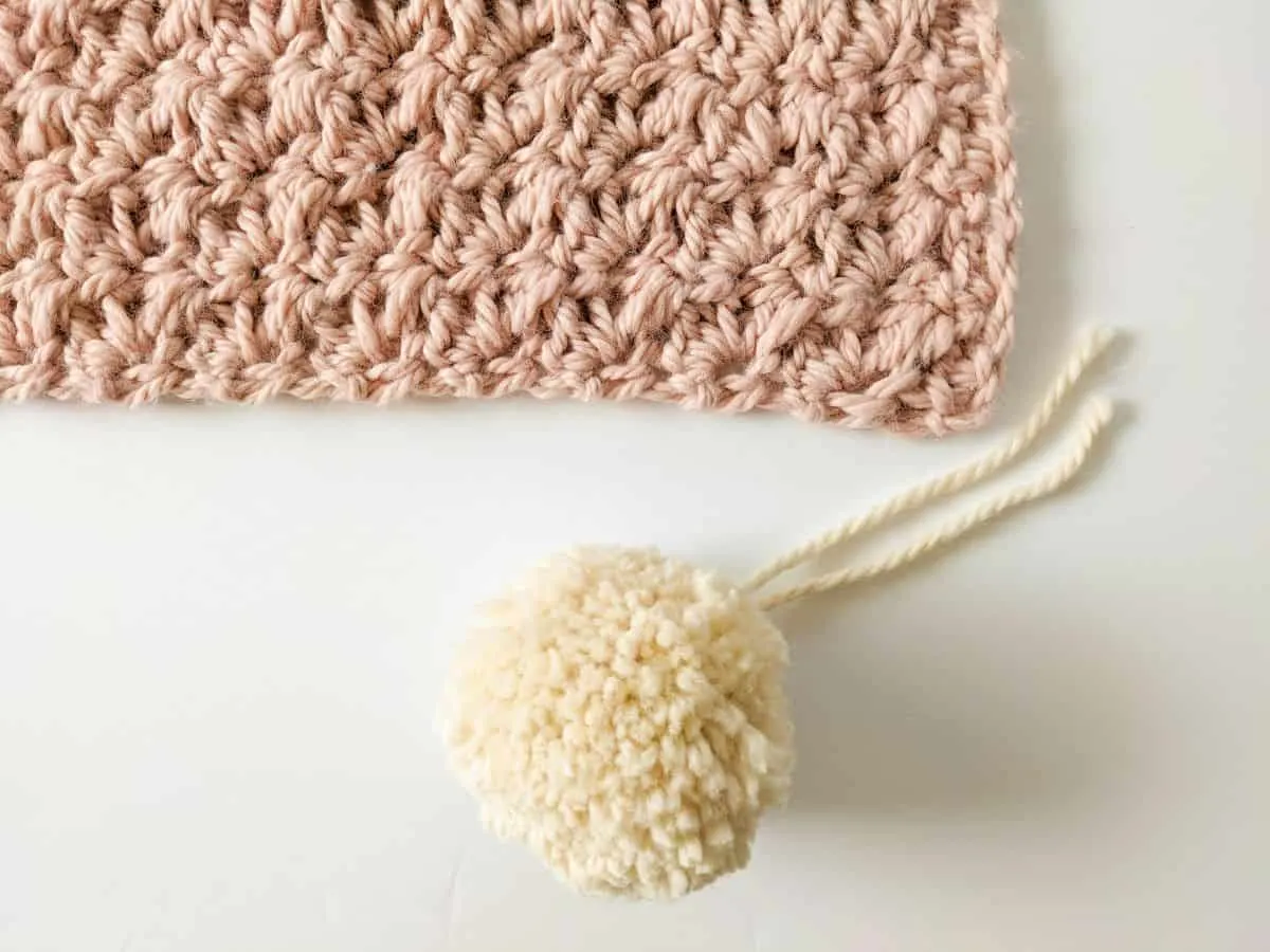 Image shows step 1 in how to attach a pom pom to your crochet blanket.