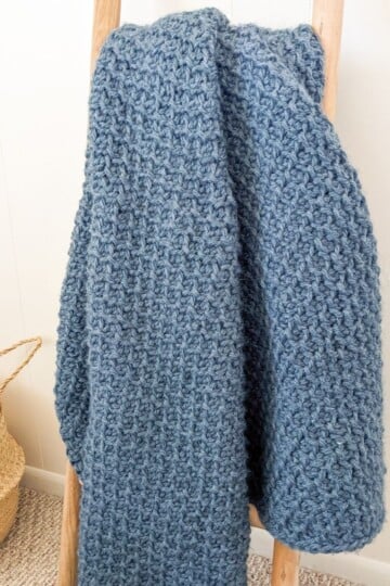 a chunky Tunisian crochet blanket on a decorative ladder.