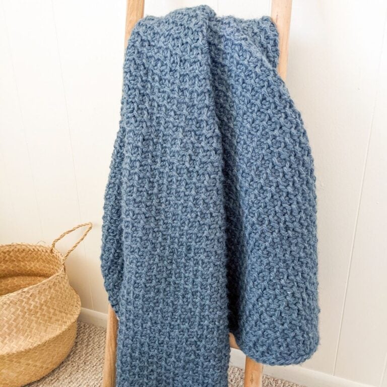 a chunky Tunisian crochet blanket on a decorative ladder.