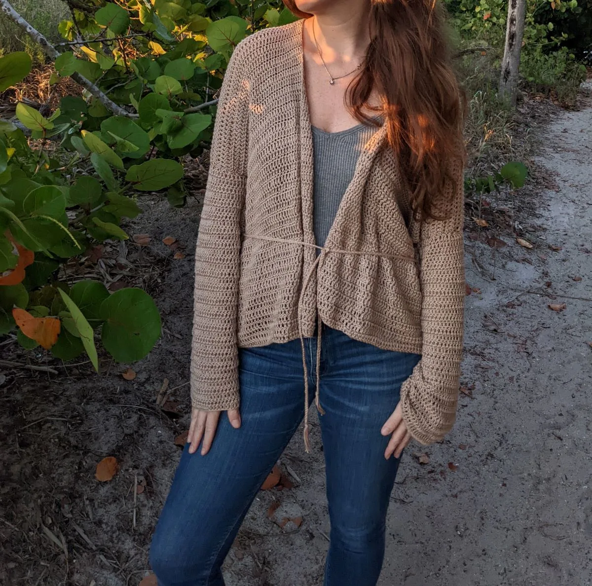model wearing a lightweight crochet cardigan with a strap around the waist.