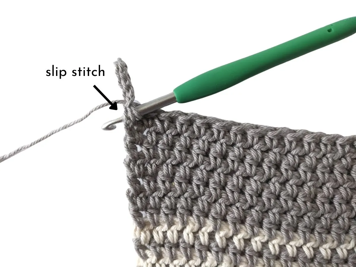 A crochet hook inserted into the corner edge of a crochet dish towel.