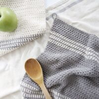 Crochet kitchen towels in grey and white with a wooden spoon and appel.