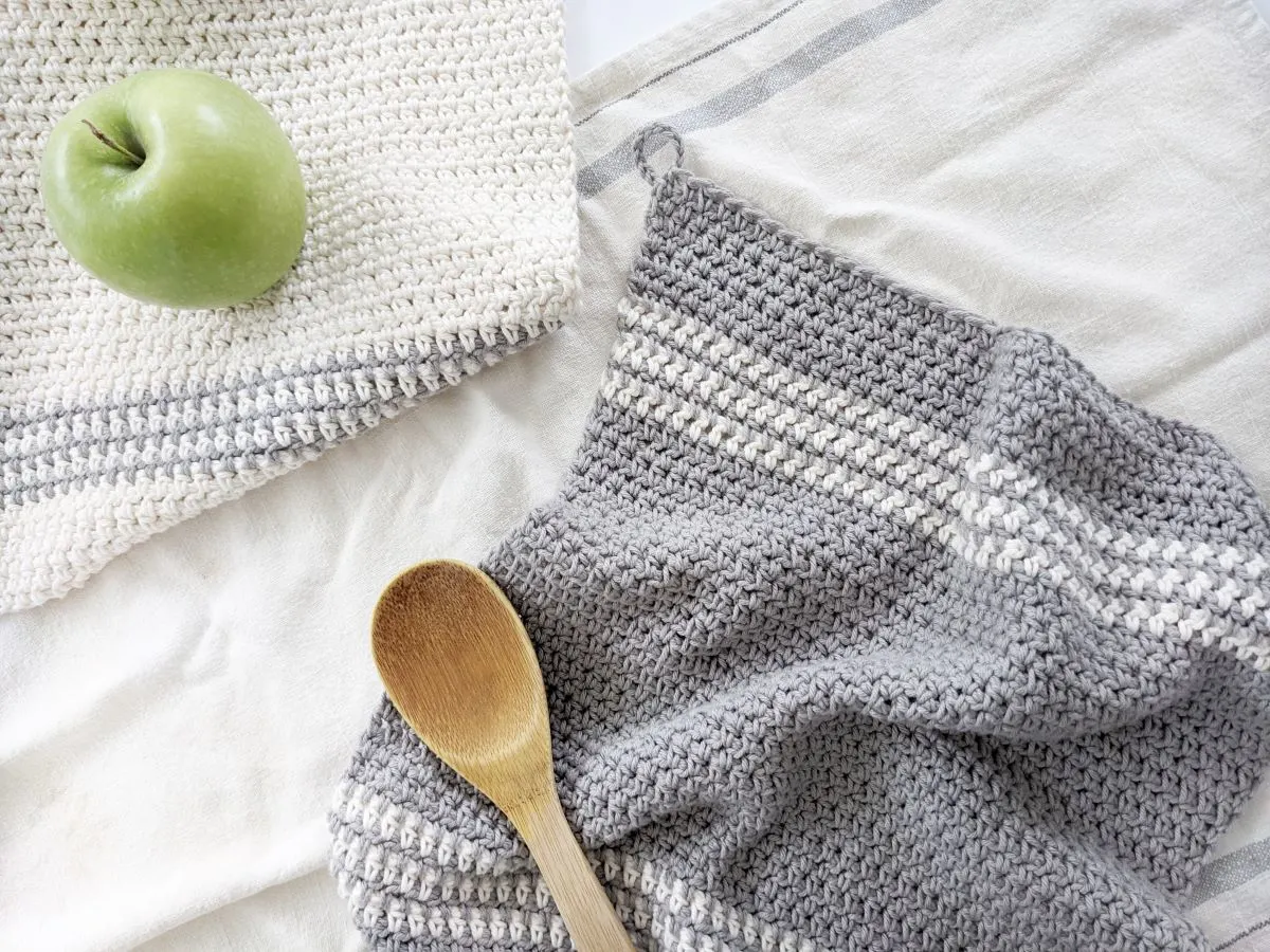 A striped crochet kitchen towel with a wooden spoon and an apple.