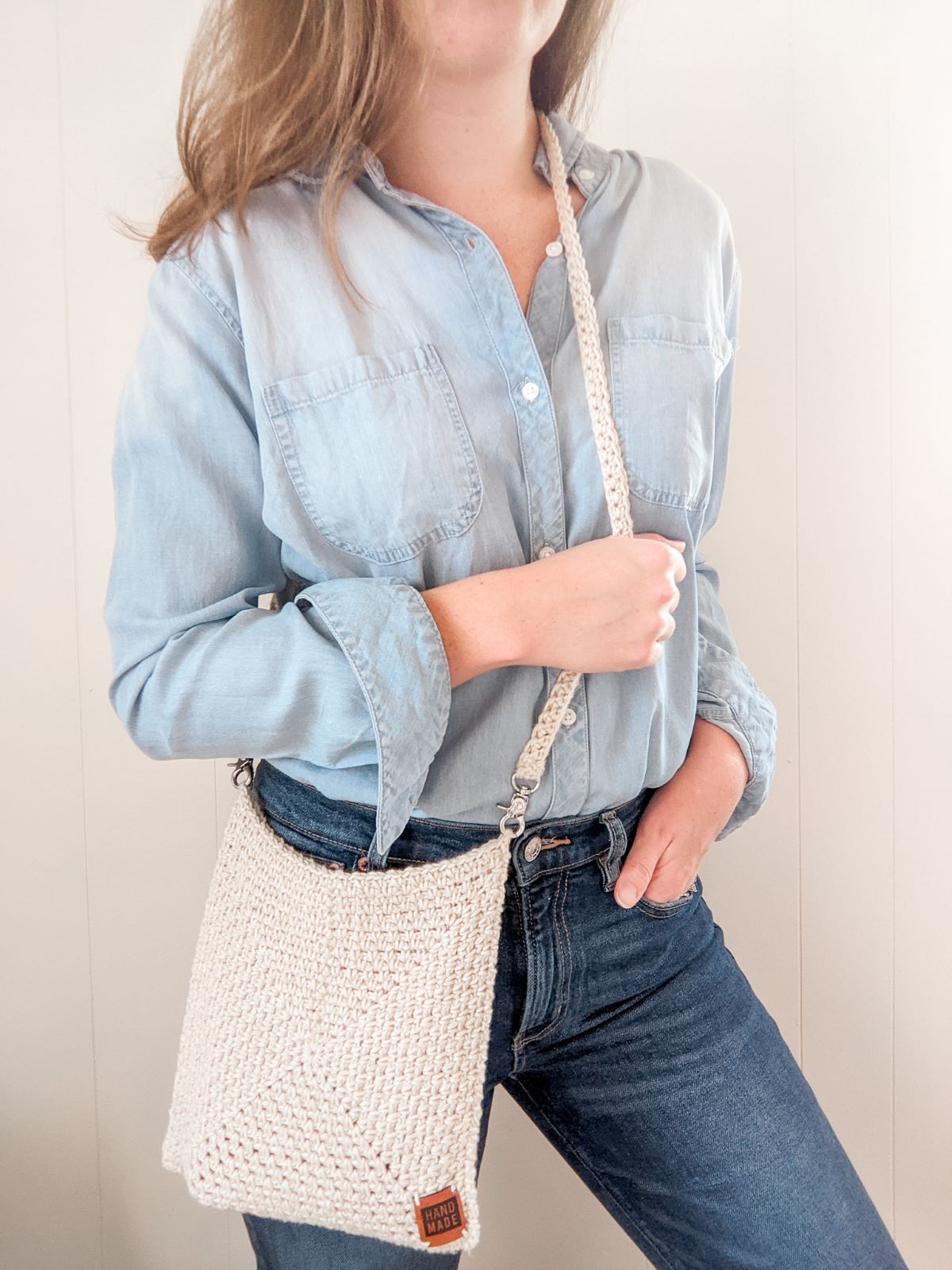 Model is wearing a crochet should bag with jeans and a long sleeve shirt.