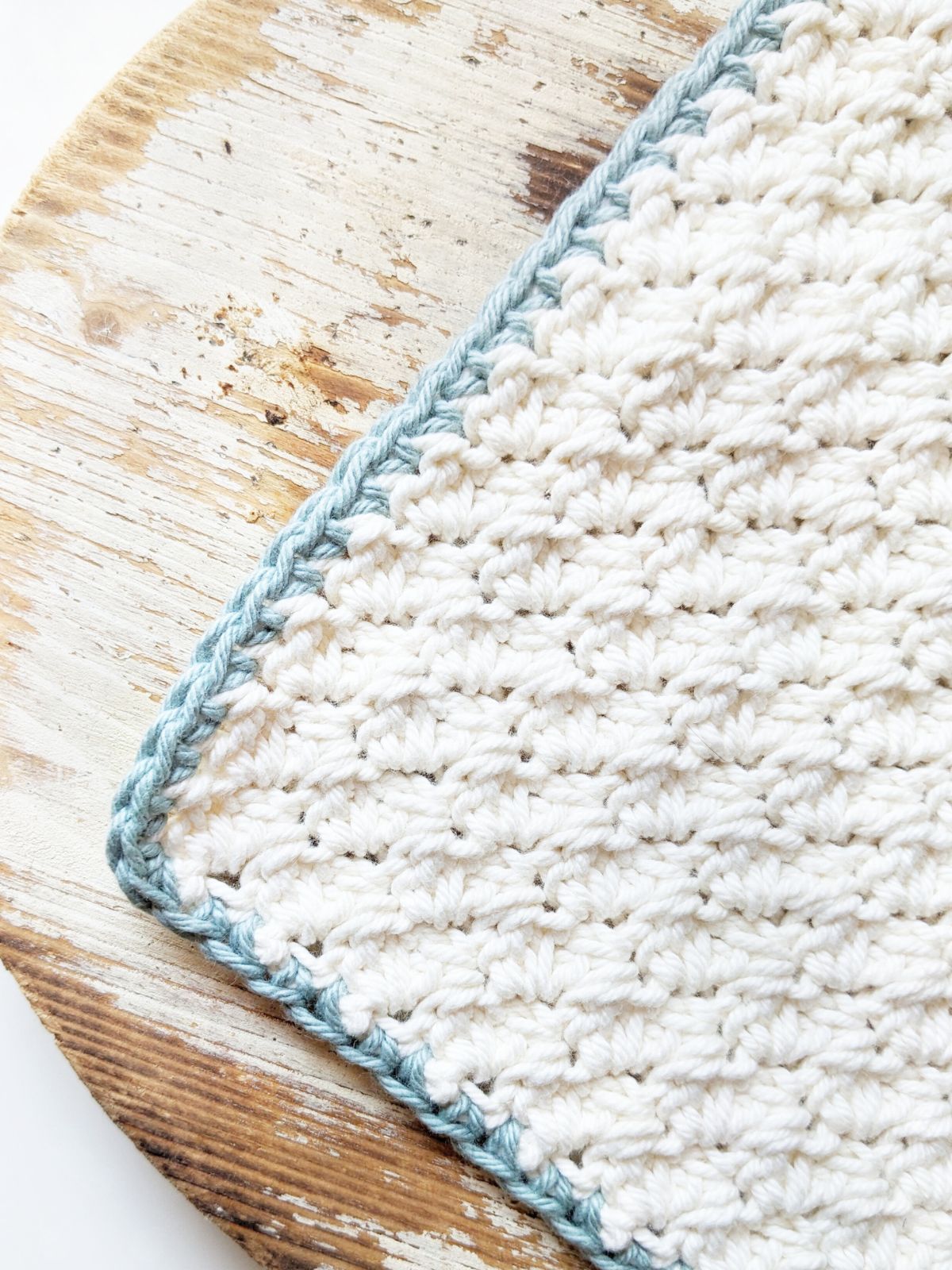 A crochet washcloth with a single crochet border on a wooden circular plank.