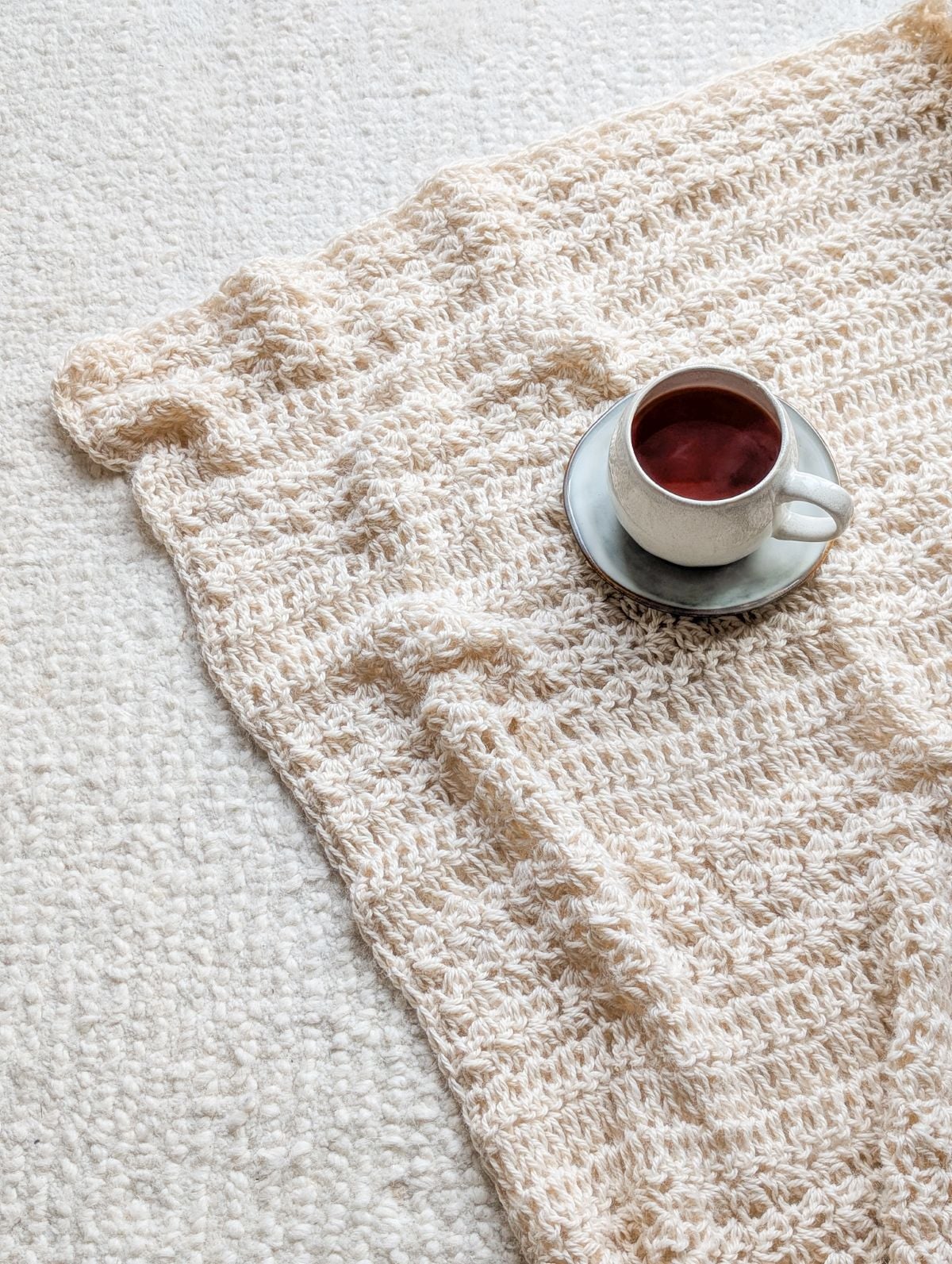 A large oversized crochet throw on a carpet with a cup of tea.