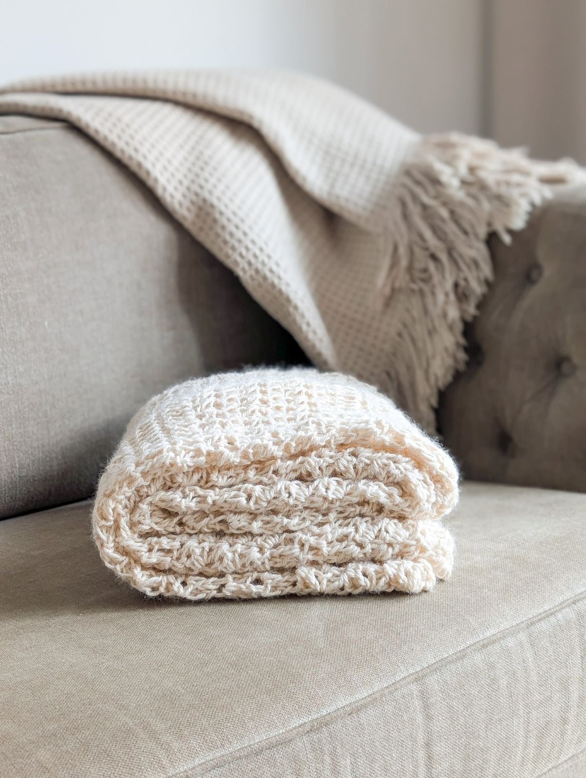 A folded crochet blanket on a couch.