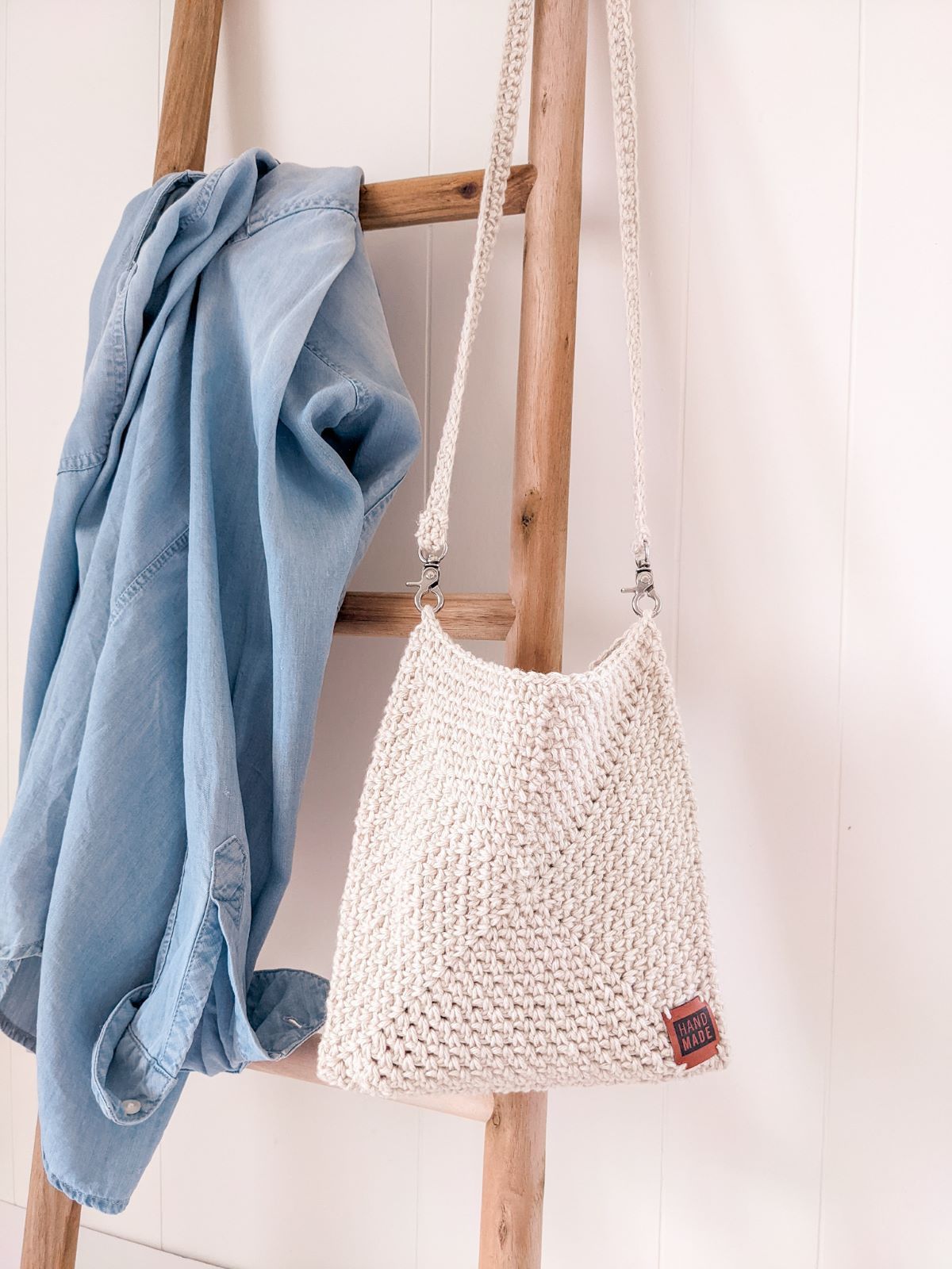 A crochet crossbody bag hanging on a decorative latter. 