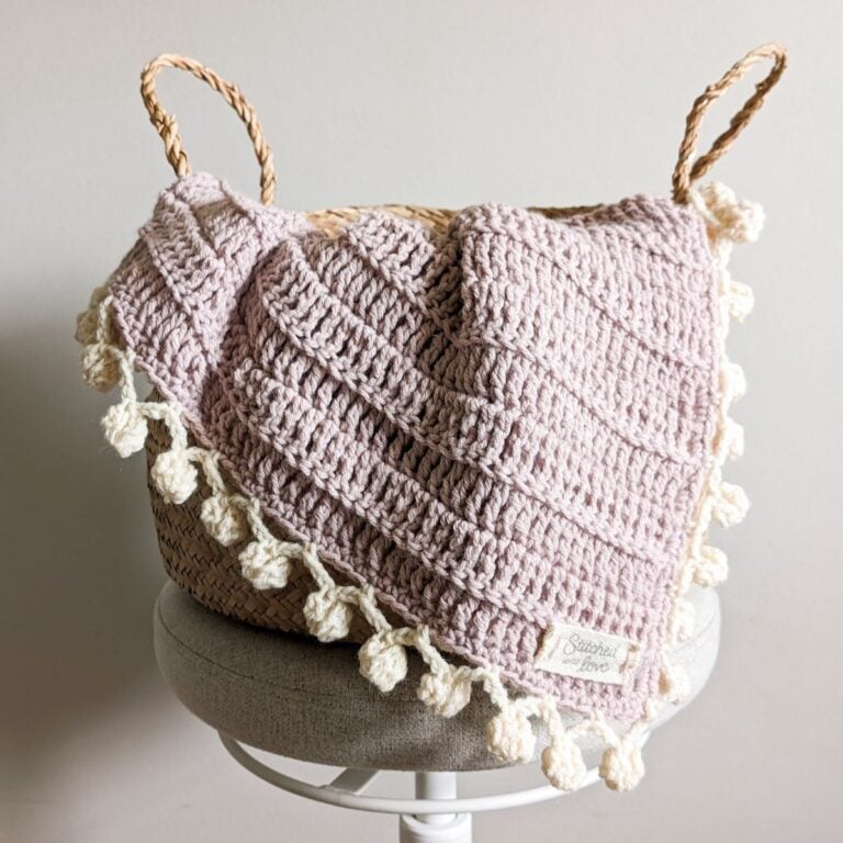 A crochet baby blanket with a pom pom border.