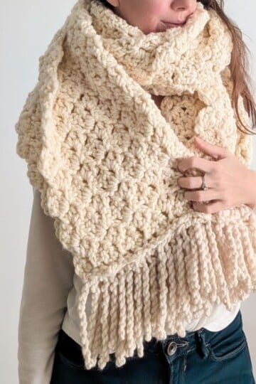 Model is wearing a chunky bulky-weight crochet blanket scarf in the color natural.