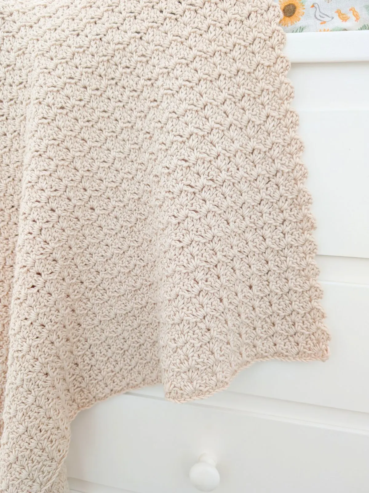 A crochet baby blanket draped over a cabinet.