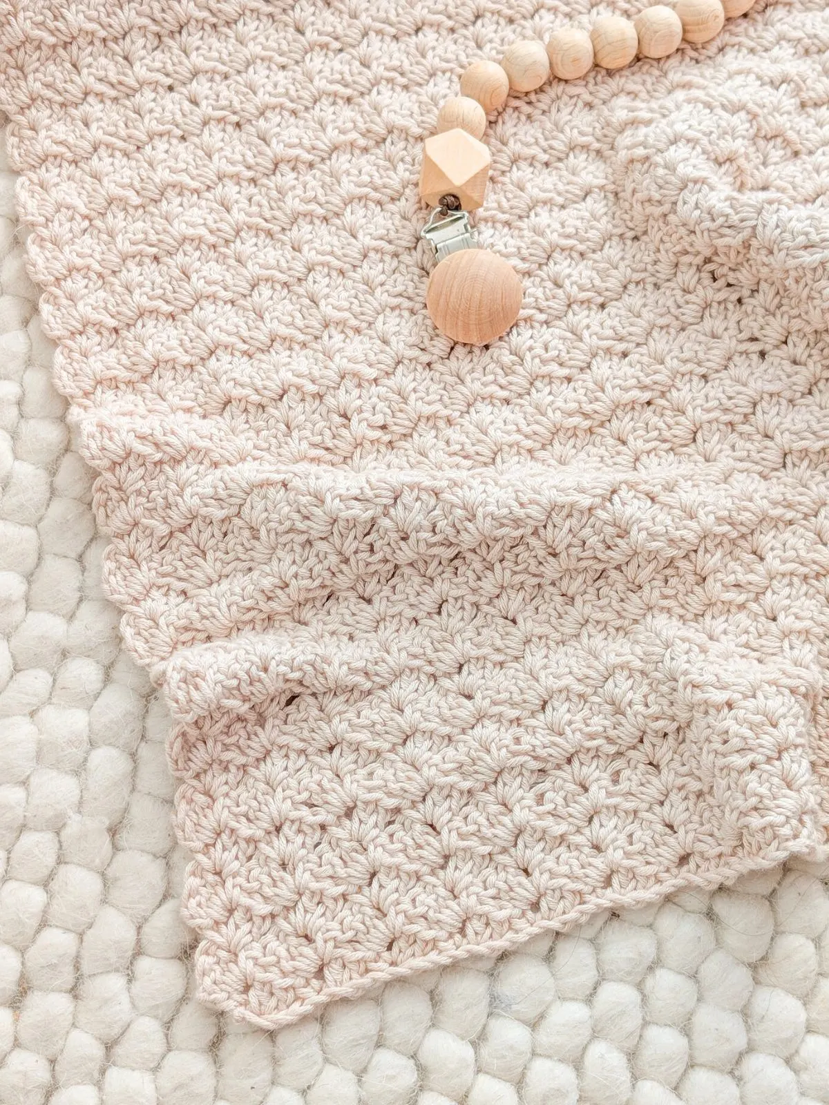 A textured crochet baby blanket with a wooden baby toy.
