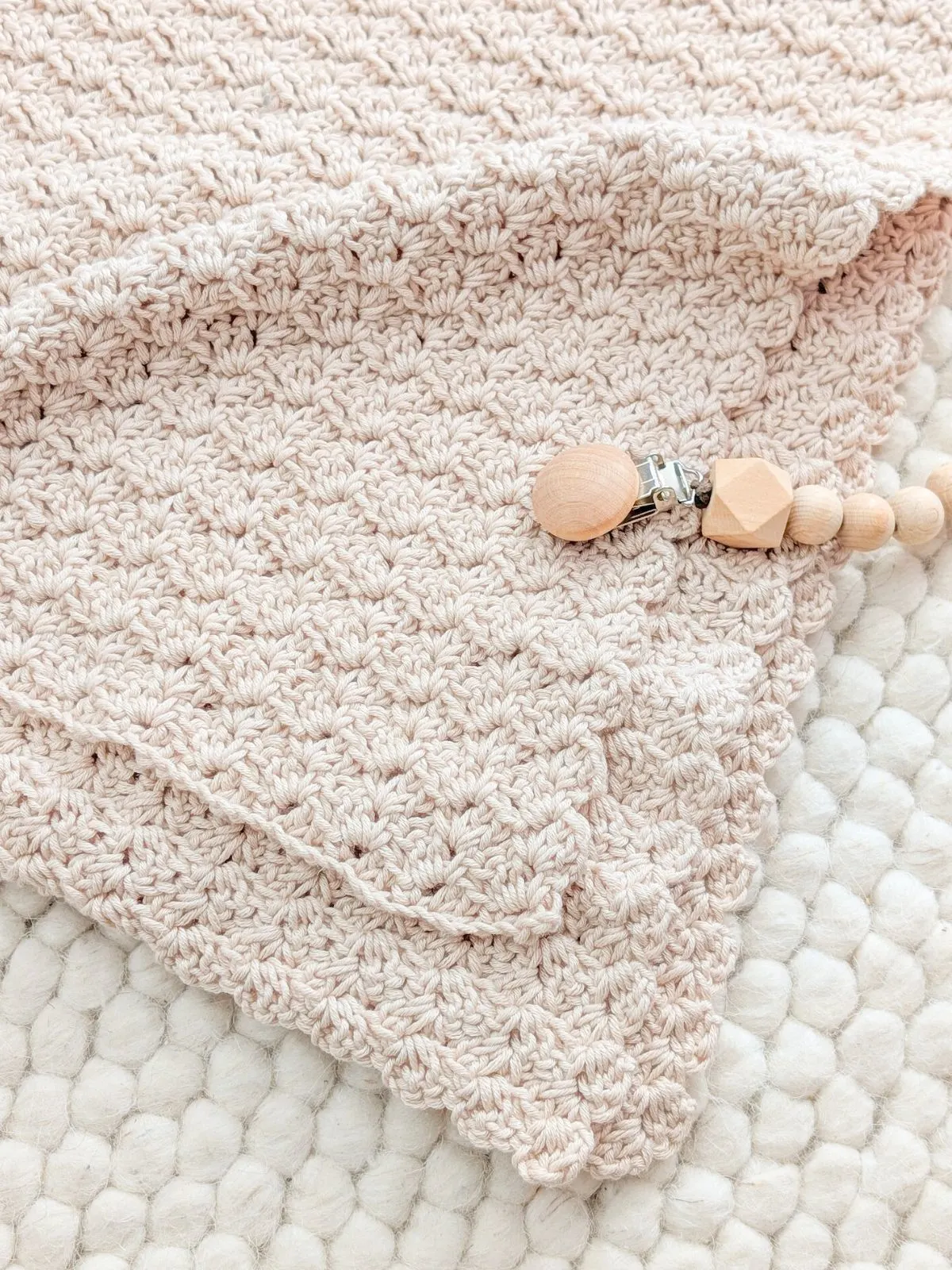 A folded crochet baby blanket with a wooden baby toy.