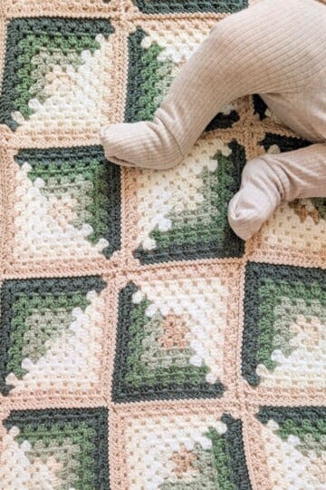 A granny square crochet baby blanket with a baby on it.