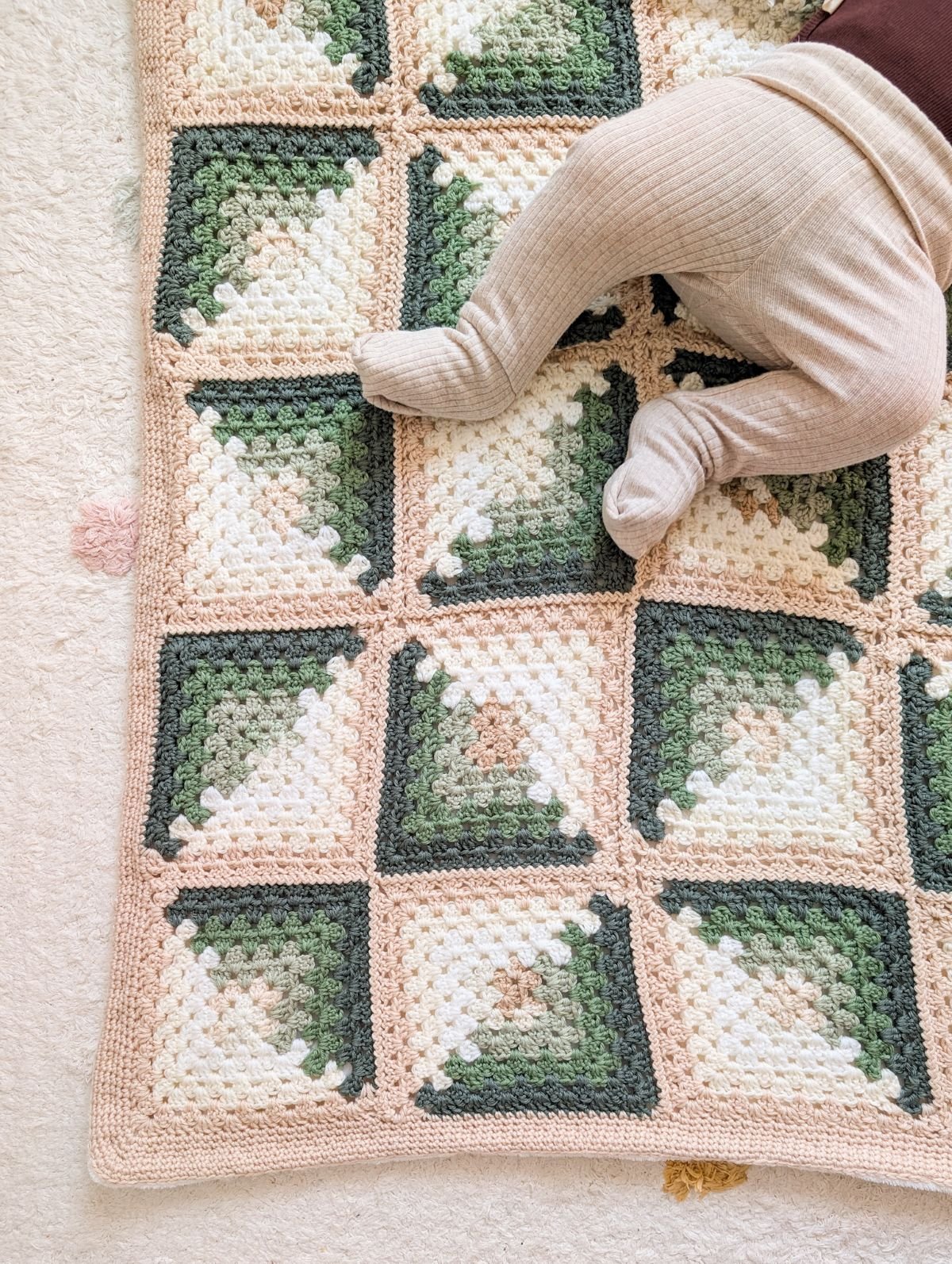 A crochet granny square baby blanket with a baby on it.
