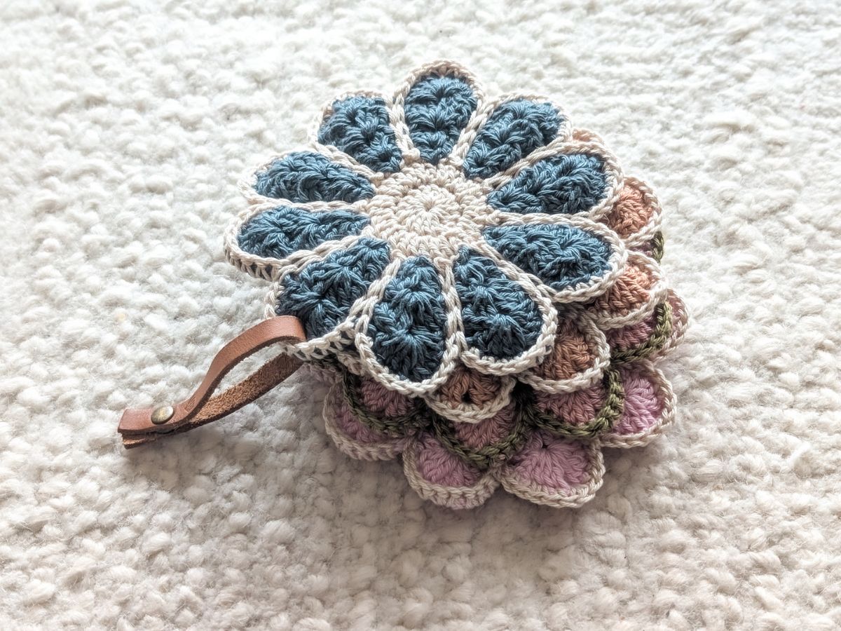 A stack of crochet flower coasters connected with a leather band.