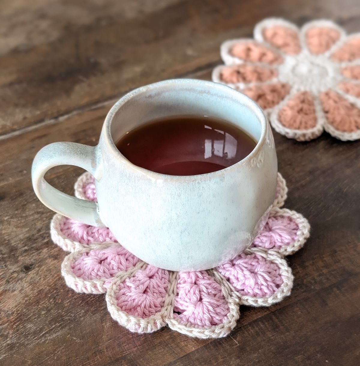 A pink crochet flower coaster with a hot cup of tea on it. 