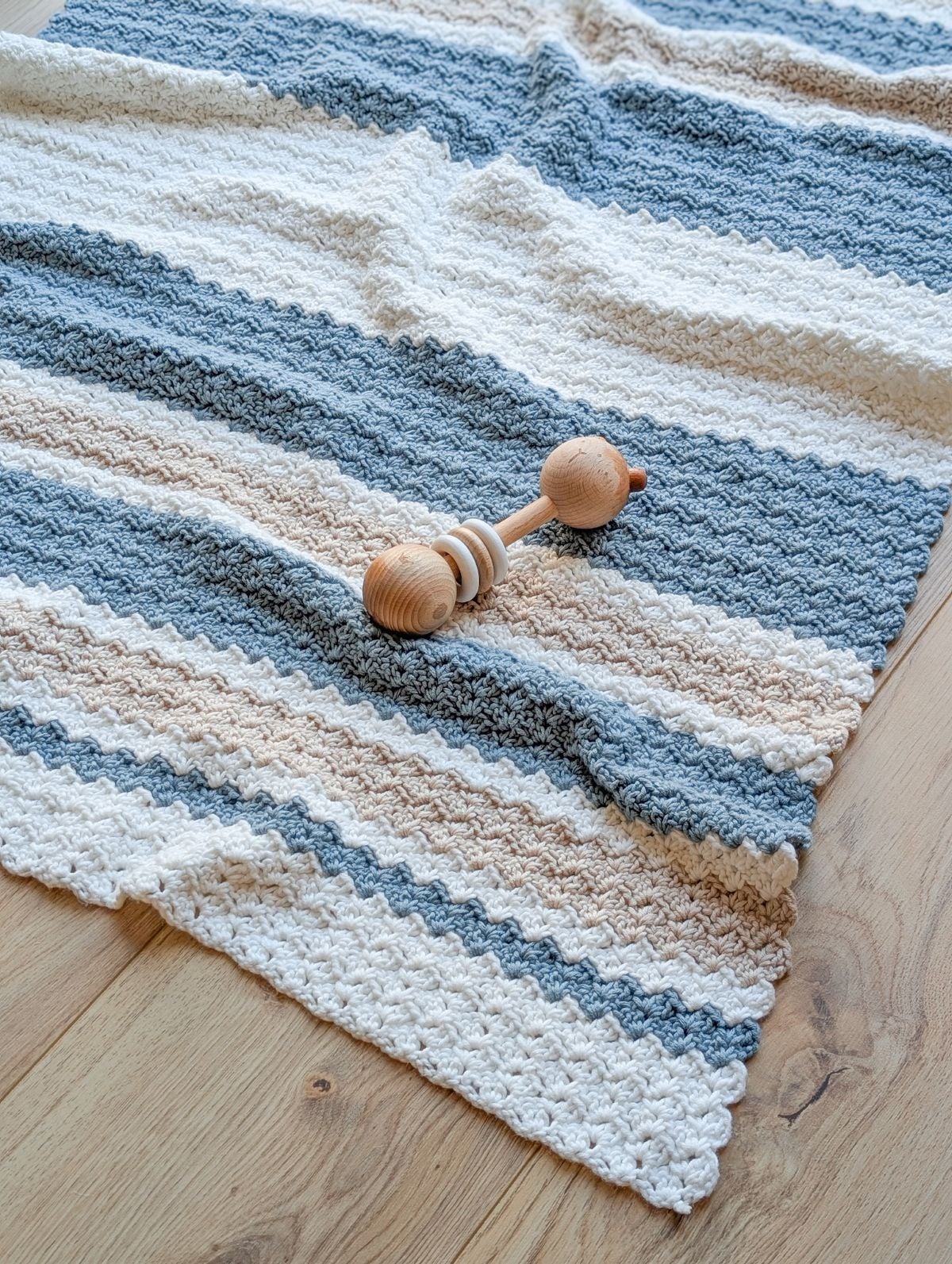 A striped crochet baby blanket layed flat on on the floor. 