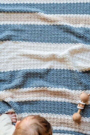 A striped crochet baby blanket in the colors blue, beige, and white.