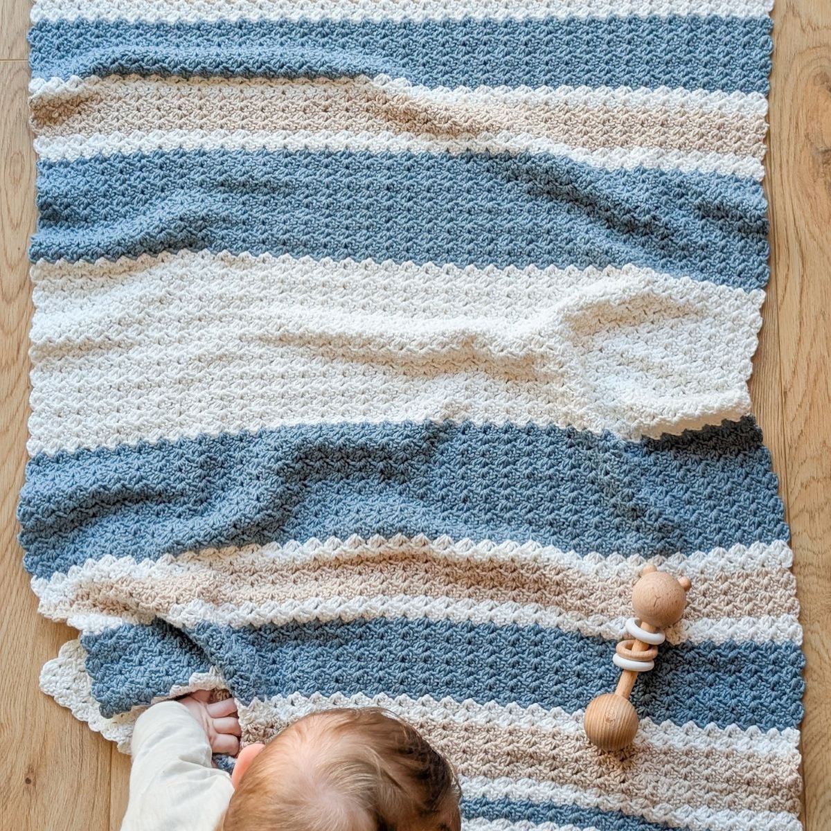 A striped crochet baby blanket in the colors blue, beige, and white.