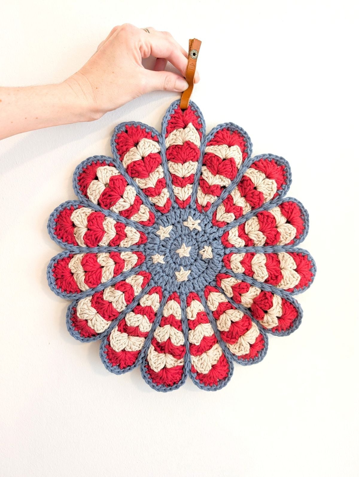 A person holding a striped crochet potholder in the shape of a flower.
