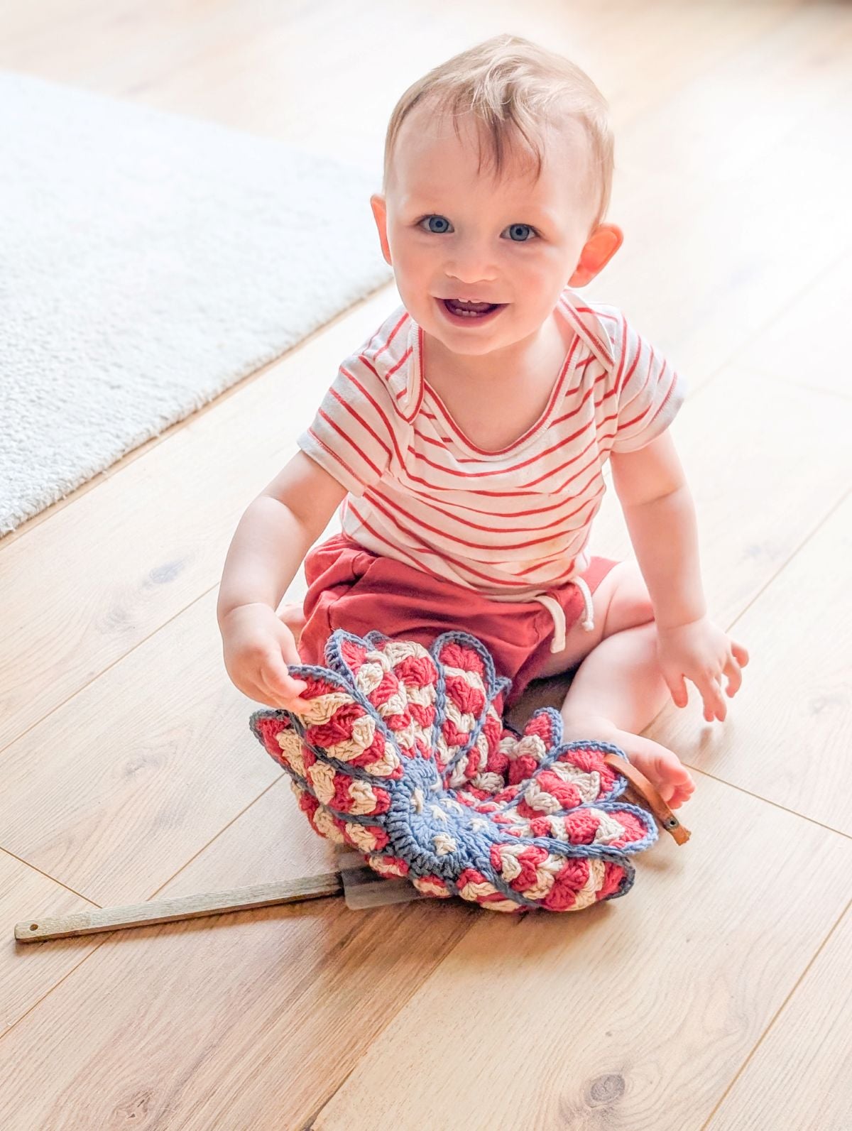 A baby holding a crochet flower potholder with a spatula.