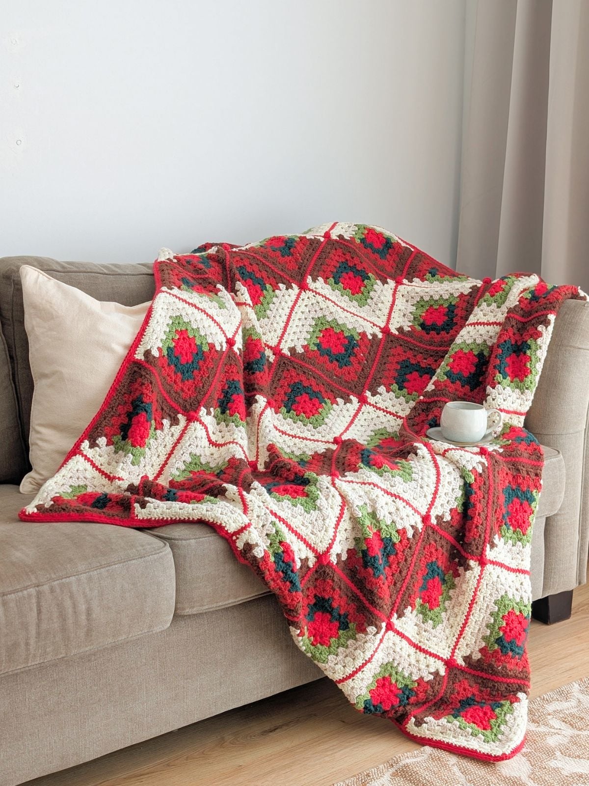 A crochet granny square blanket in Christmas colors on a couch.