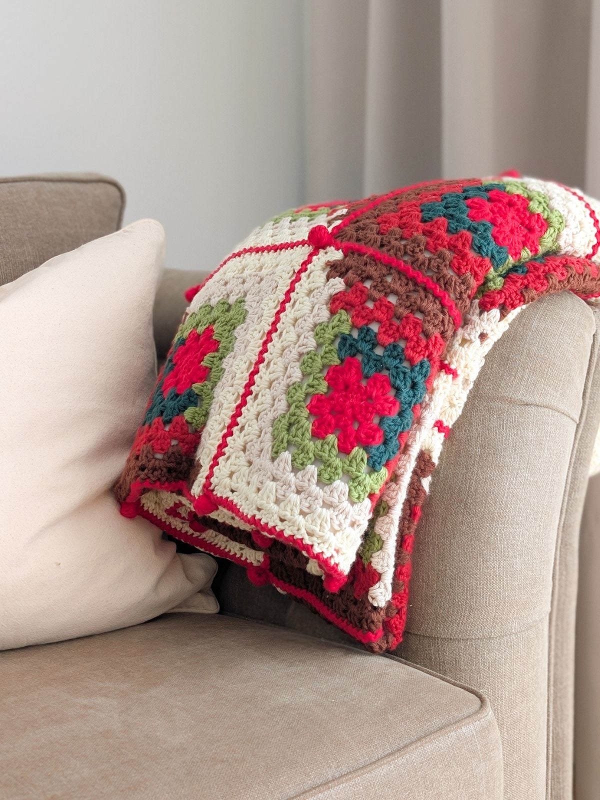 A large folded crochet granny blanket on the corner of the couch. 