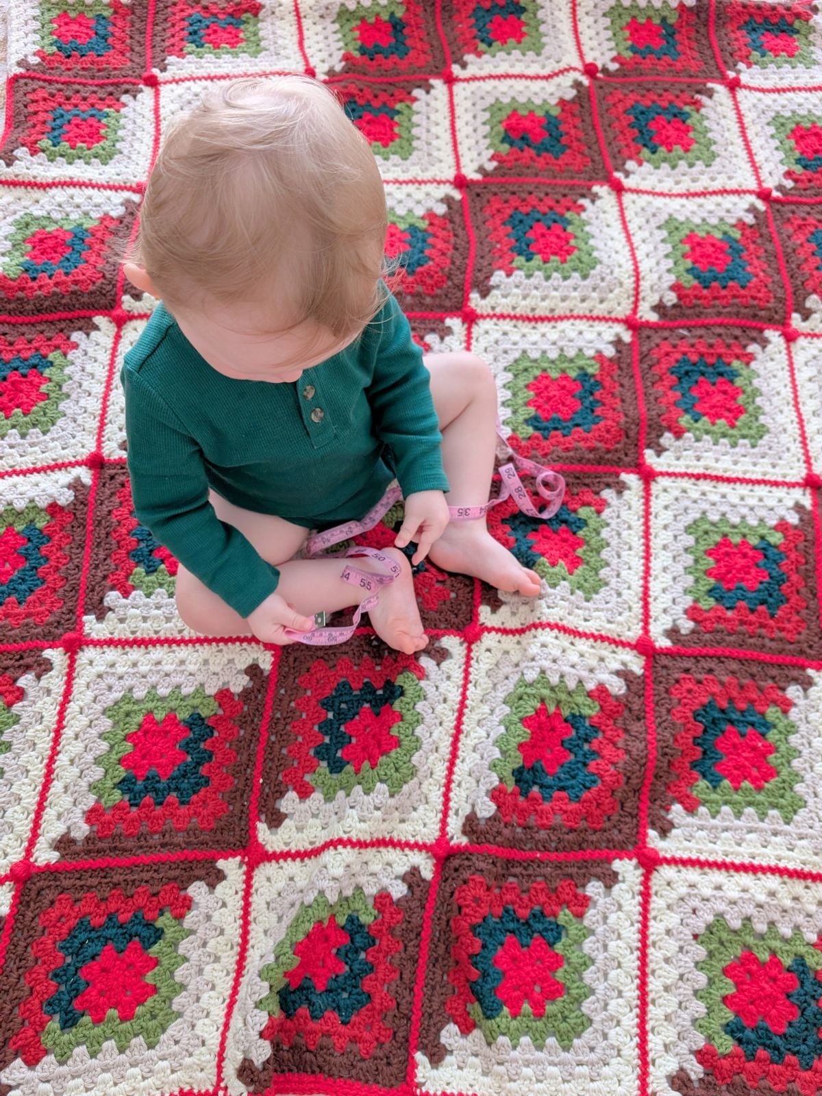 A toddler on a crochet Christmas blanket.