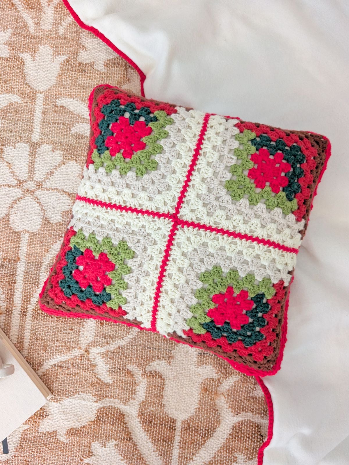 A crochet Christmas themed pillow on a carpet.