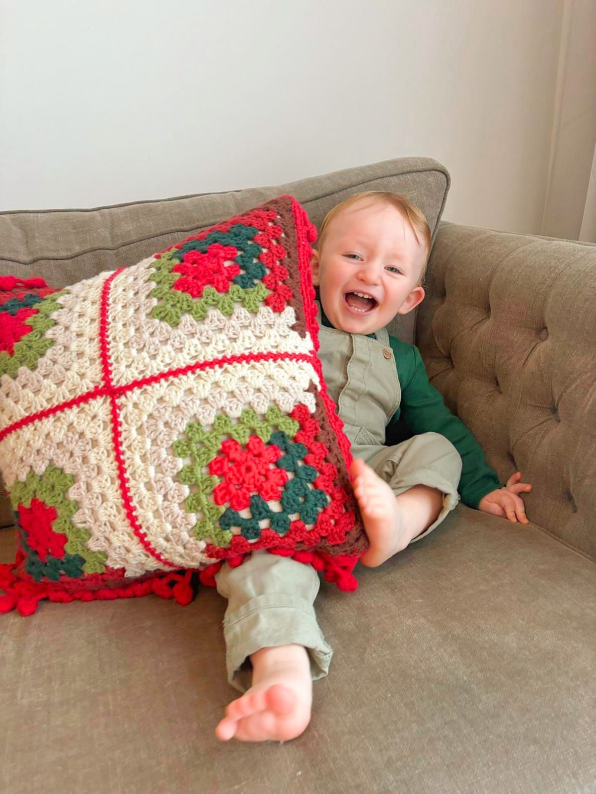 A toddler holding a crochet granny square pillow.