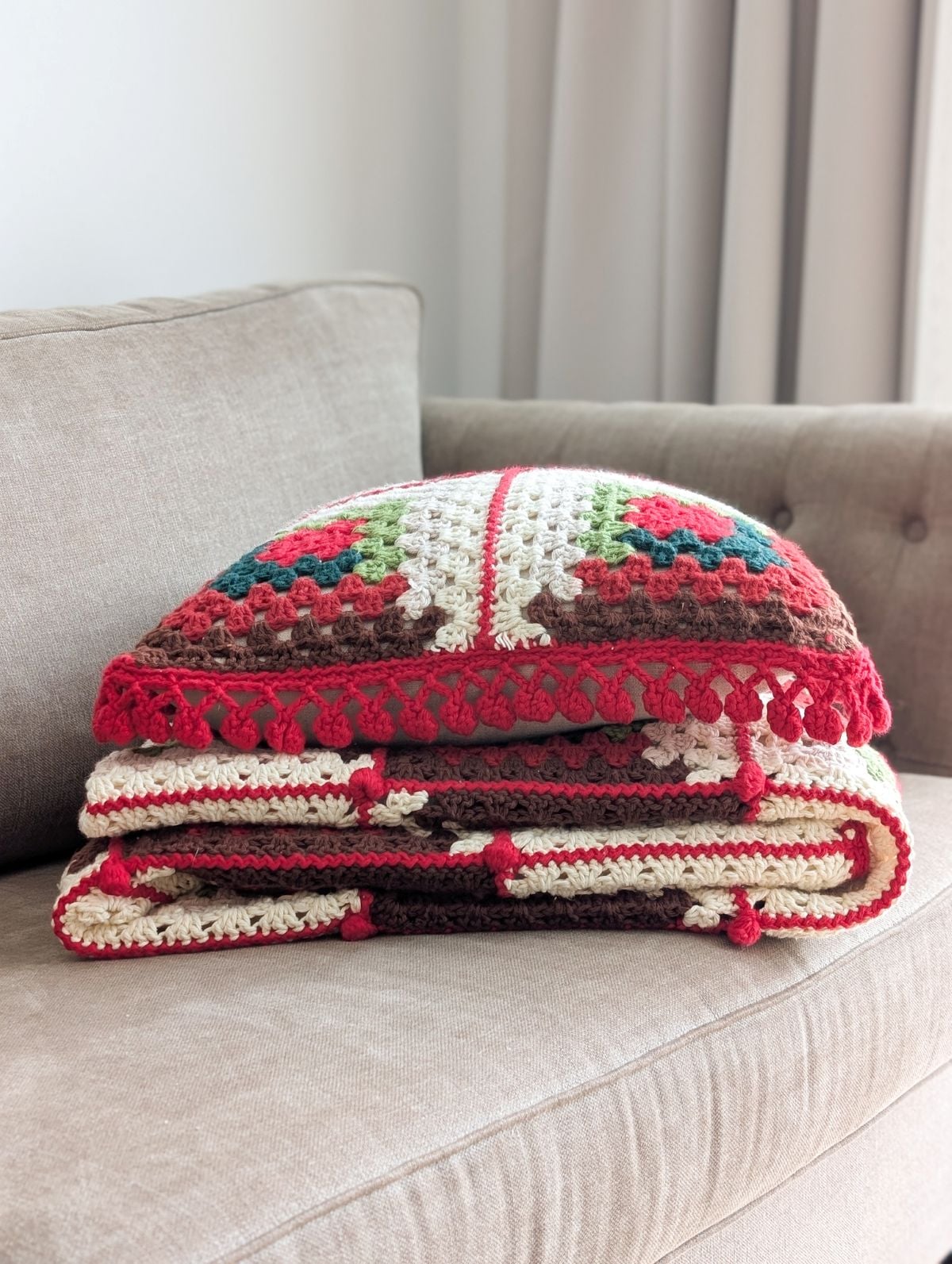 A crochet Christmas blanket and pillow folded on the couch.