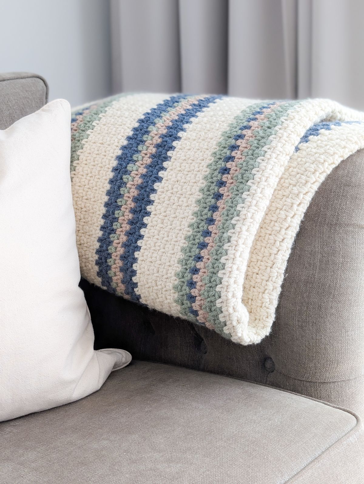 A folded crochet blanket in different colors on the couch.